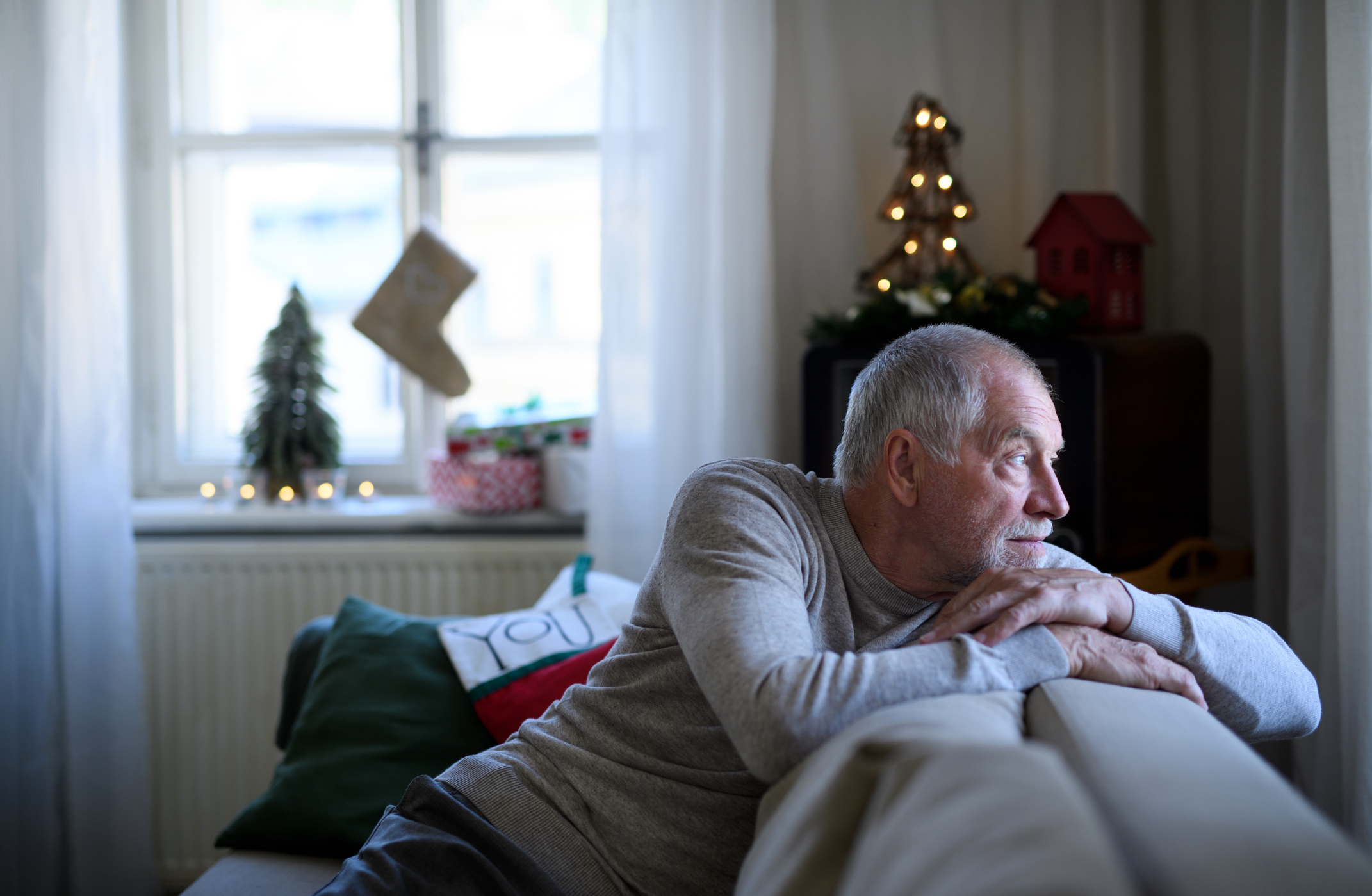 Older man looking at window with holiday decorations in background.