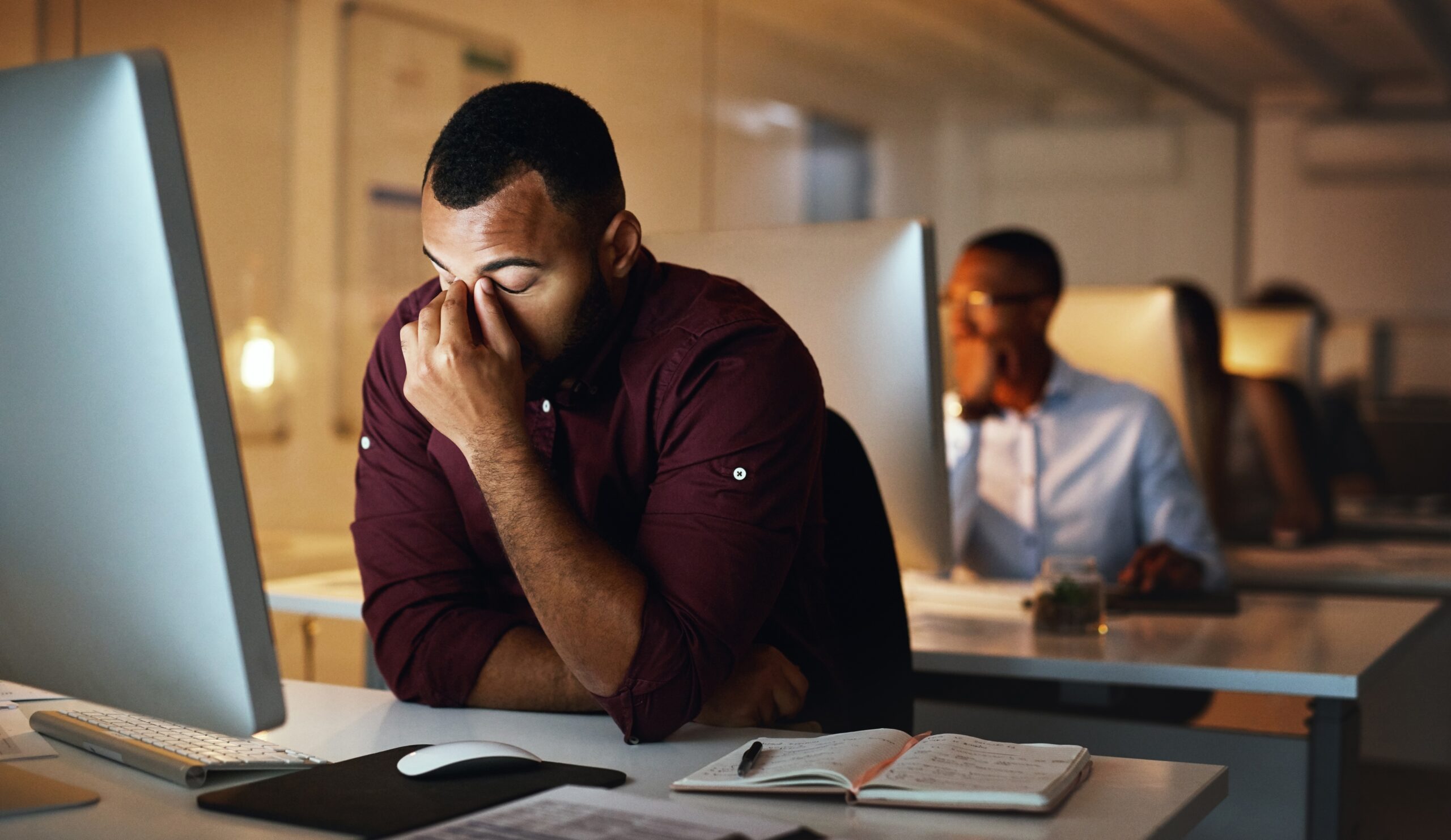 Man working late in an office experiencing burnout, with elbows on desk resting his head in hand